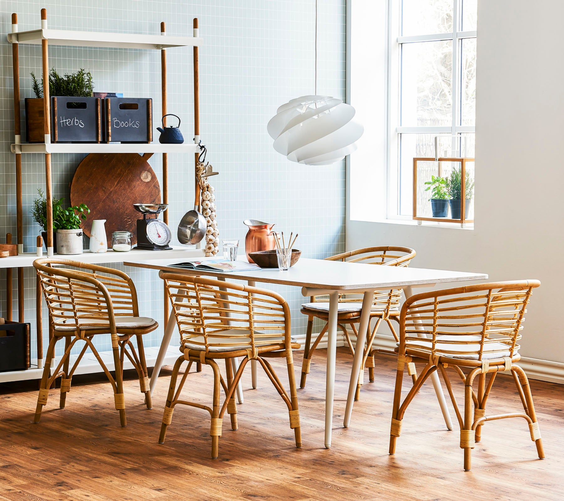 Et stilfuldt spisestueområde med et lyst træbord omgivet af rattanstole og en moderne pendellampe, suppleret med dekorative hylder.