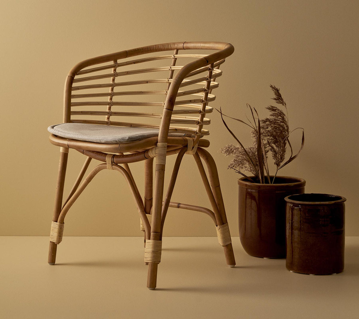 En stilfuld rattan stol med polstret sæde, ledsaget af to dekorative krukker med tørrede planter.