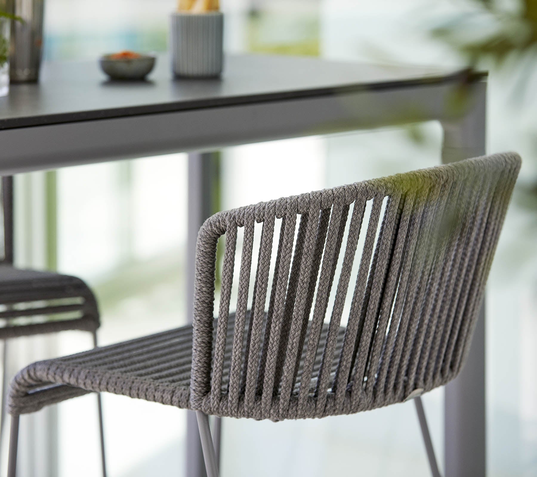 Stilfuld grå stol med et slankt design, der har vertikale striber og en moderne æstetik, placeret ved siden af et minimalistisk bord.
