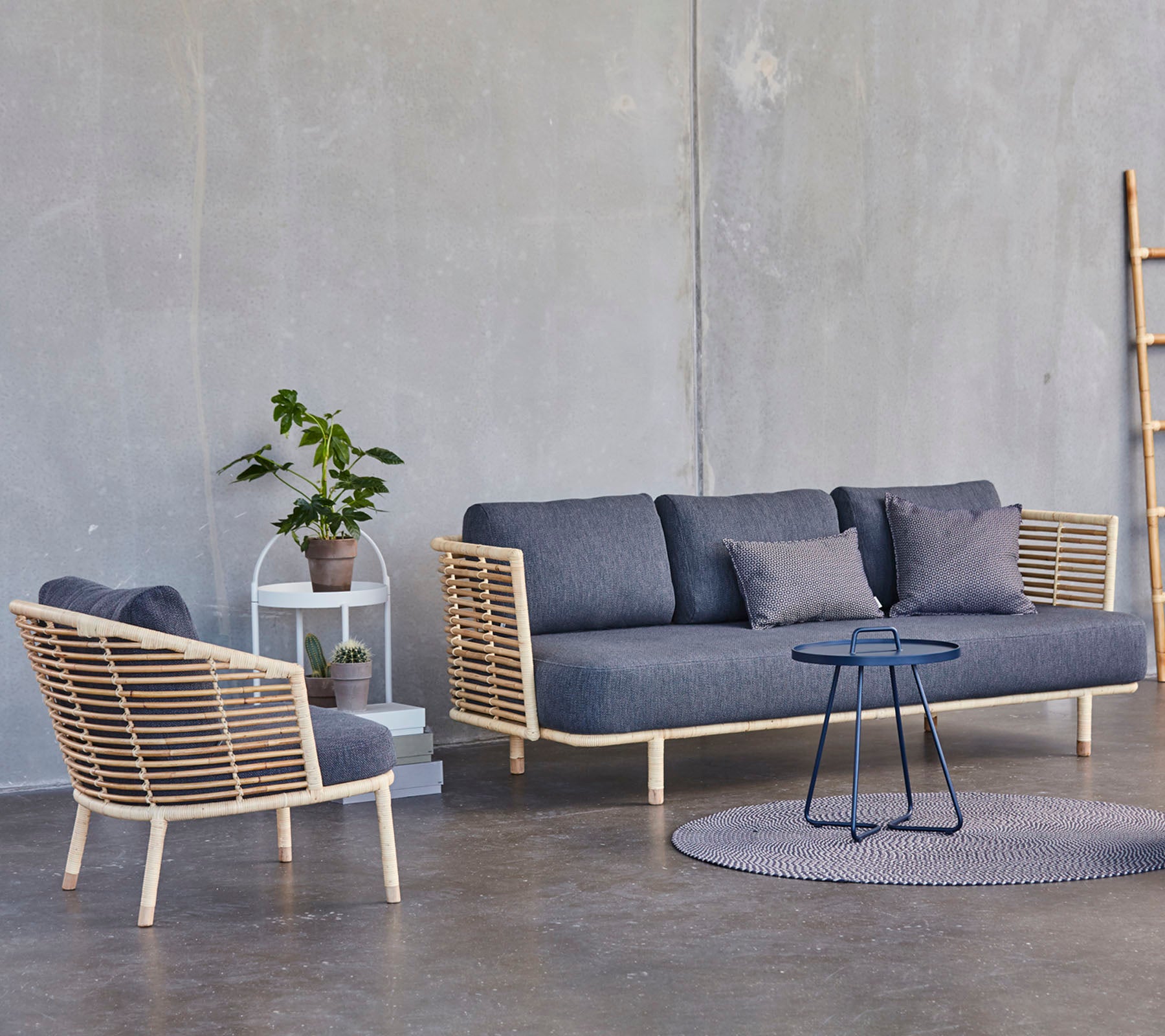 Et moderne siddearrangement med en stilfuld sofa og lænestol med trædetaljer, ledsaget af et lille sidebord og en potteplante.