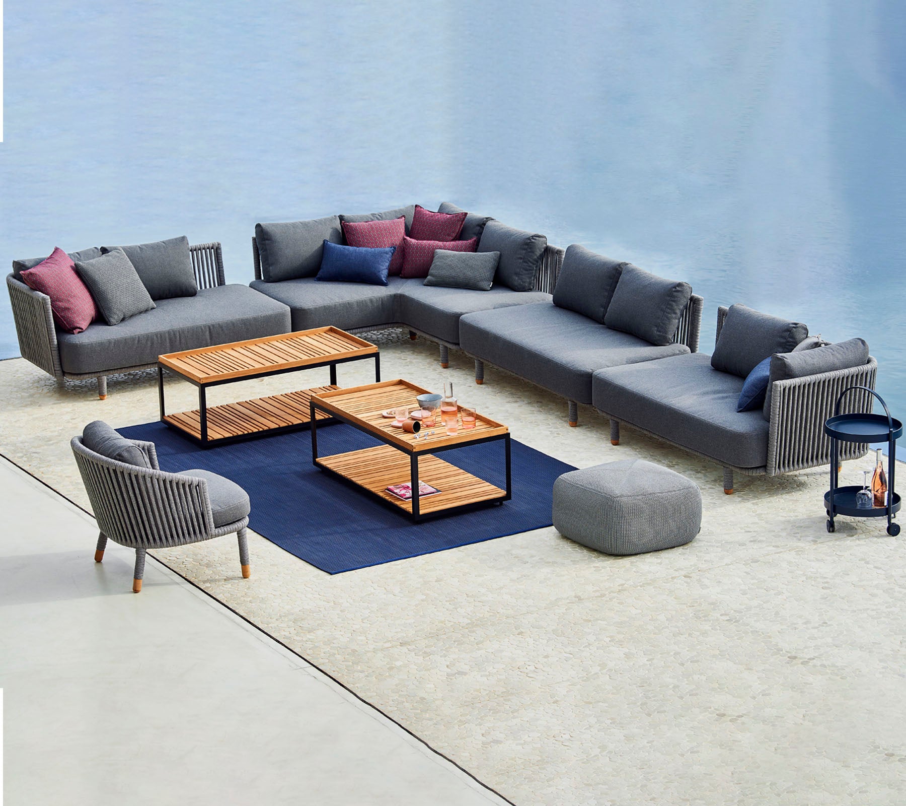 Moderne siddearrangement med en modulær grå sofa med farverige puder, sofaborde og en matchende accentstol.