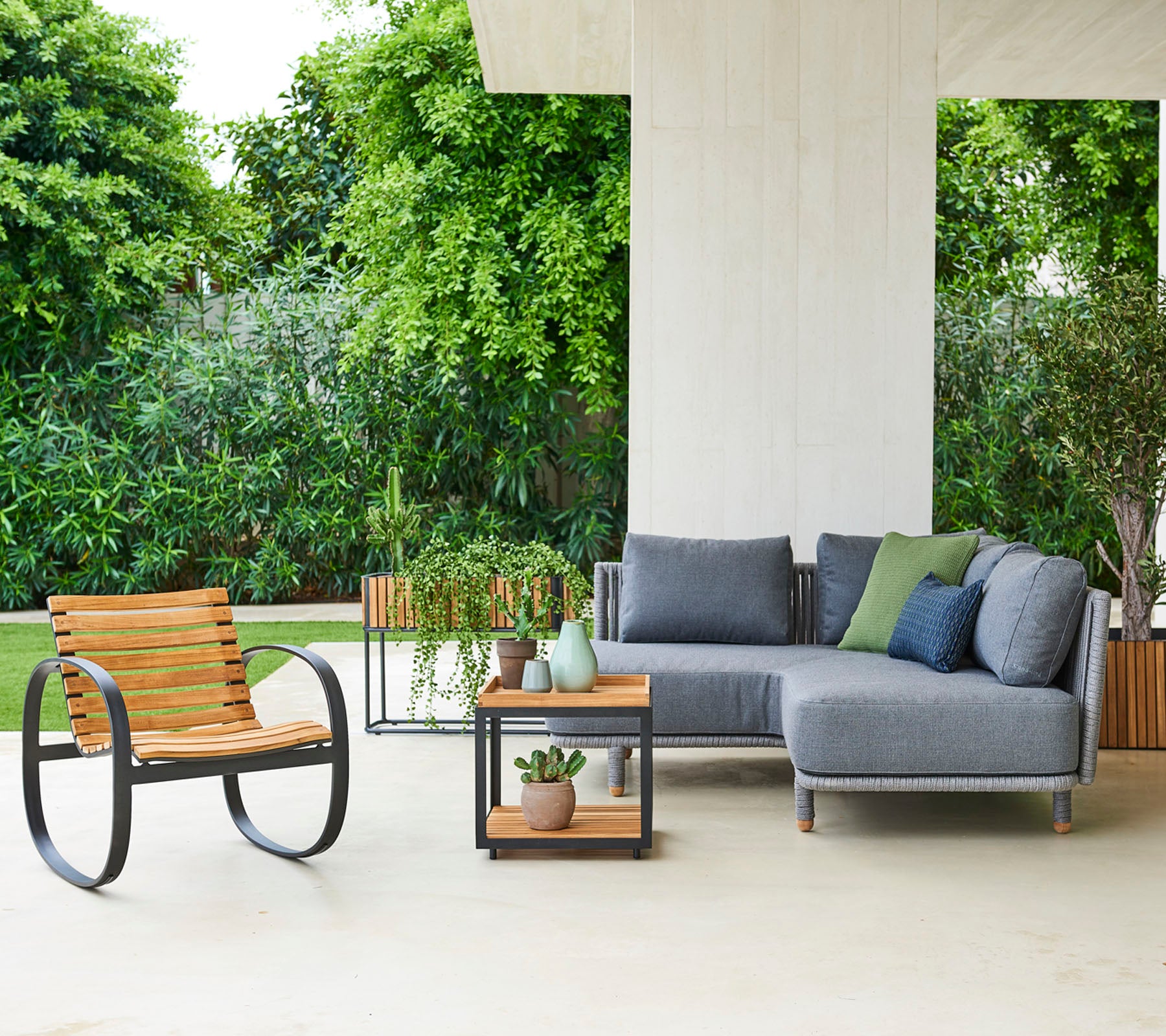 Moderne siddearrangement med en modulsofa med puder, en stilfuld stol og et sidebord med dekorative planter.