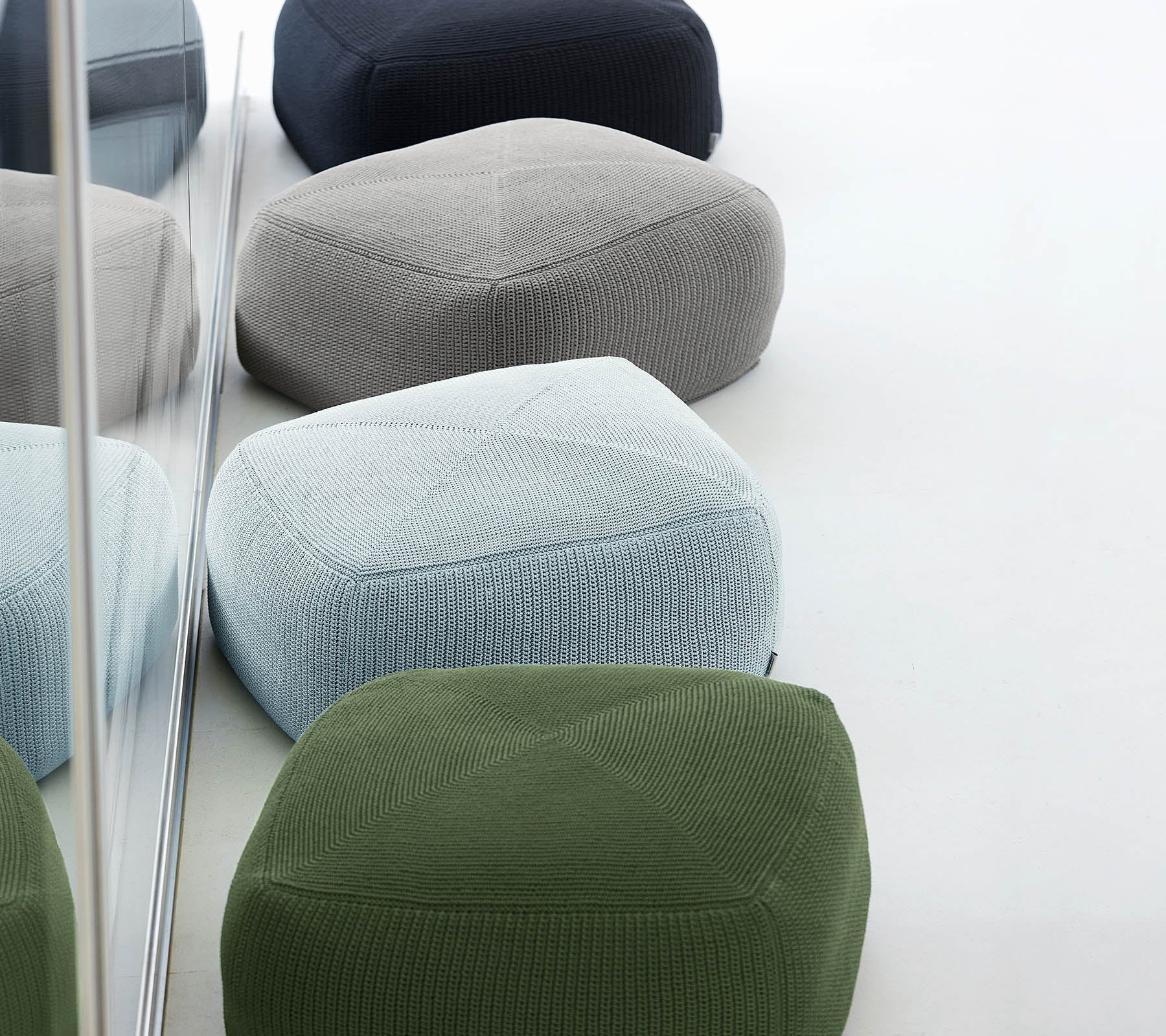 En samling af farverige, teksturerede poufs i forskellige nuancer, arrangeret sammen, der afspejler stilfuld og moderne design.