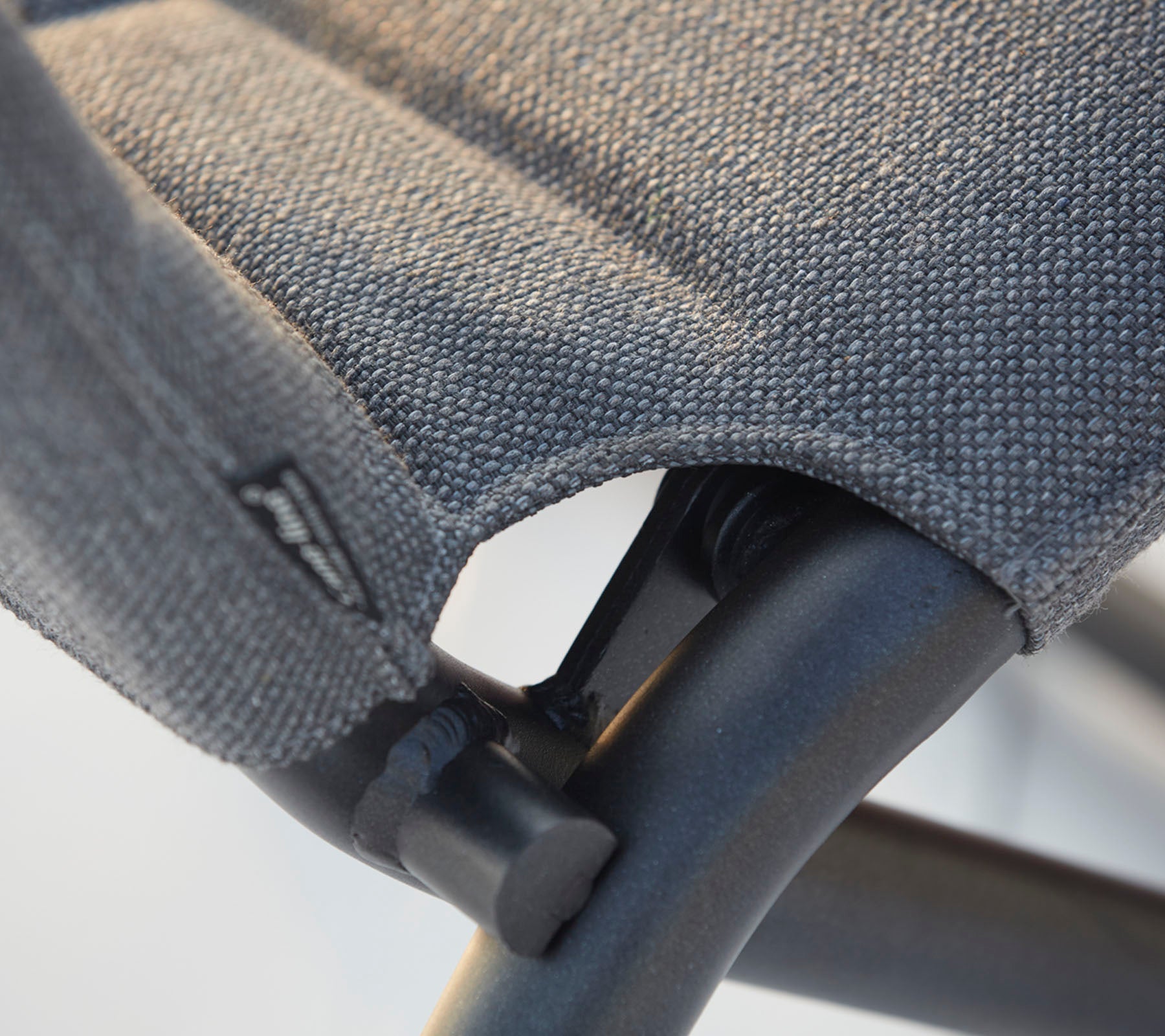 Nærbillede af en stol med tekstureret stofsæde og solid sort ramme, der fremhæver syningerne og design detaljer.