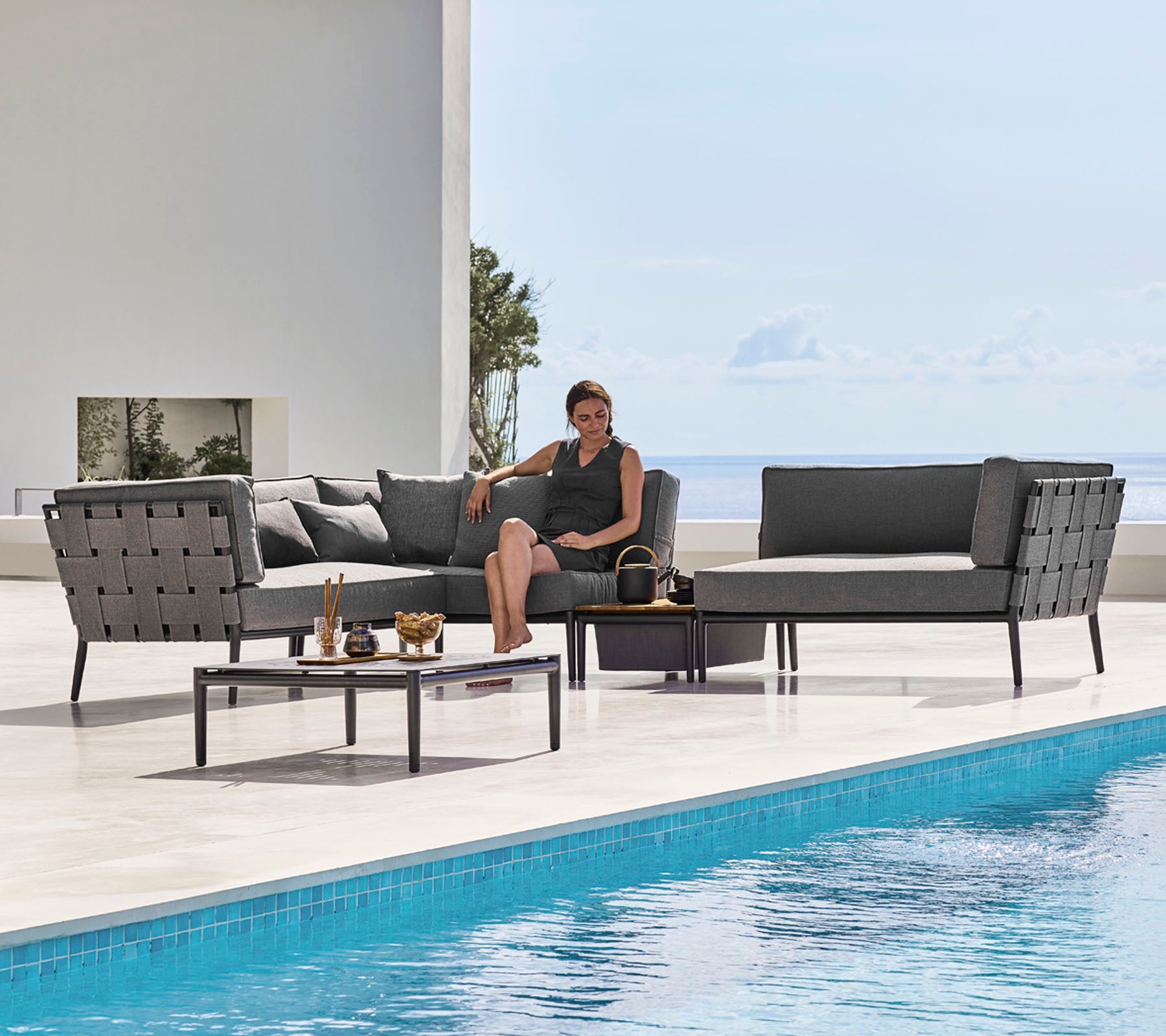 Et stilfuldt udendørs lounge sæt med elegante siddepladser og et glasbord ved siden af en pool, med en person der slapper af behageligt.