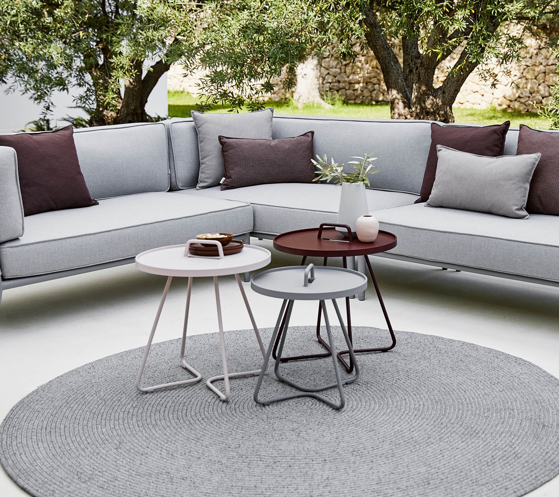 Stilfuld udendørs siddeområde med en sektion sofa med puder og moderne runde kaffeborde i en afslappet, nutidig atmosfære.