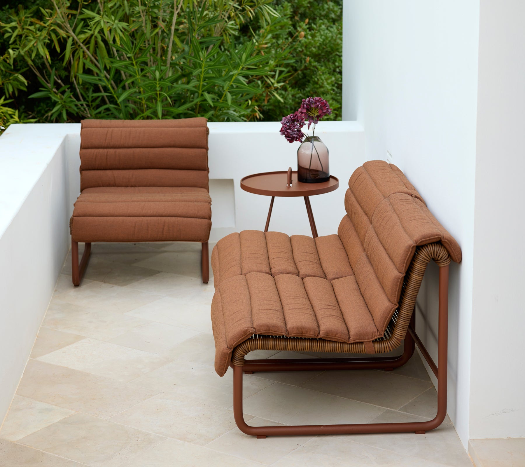 Brun lounge stol og loveseat med et rundt sidebord i en moderne udendørs indstilling.