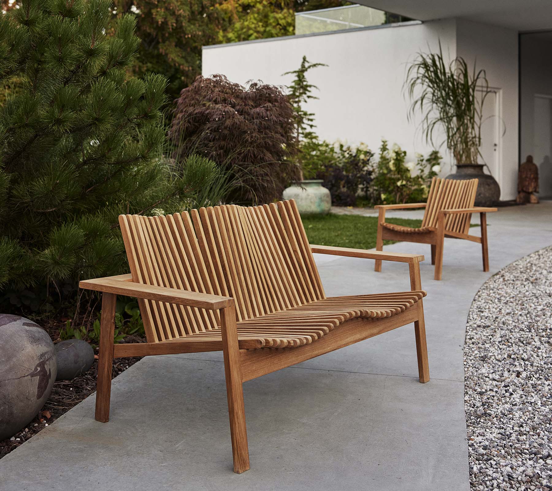 To træ-Amaze loungestole og en matchende sofa har et spalte-design, omgivet af grønne planter og dekorative elementer.
