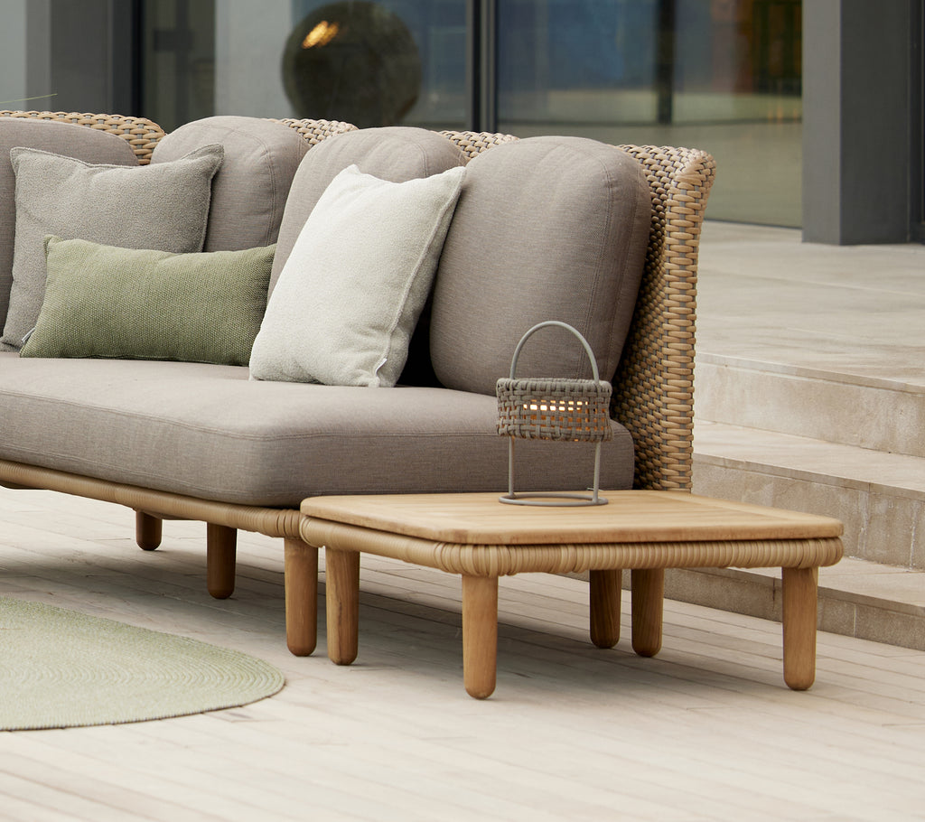Stilfuldt bueformet kaffe bord med en teak top sammen med puder på en moderne sofa, suppleret af en dekorativ Illusion lampe.