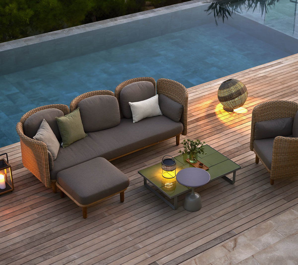 Stilfulde loungemøbler med puder, et sofabord og stemningsfyldt belysning, placeret ved en rolig pool.