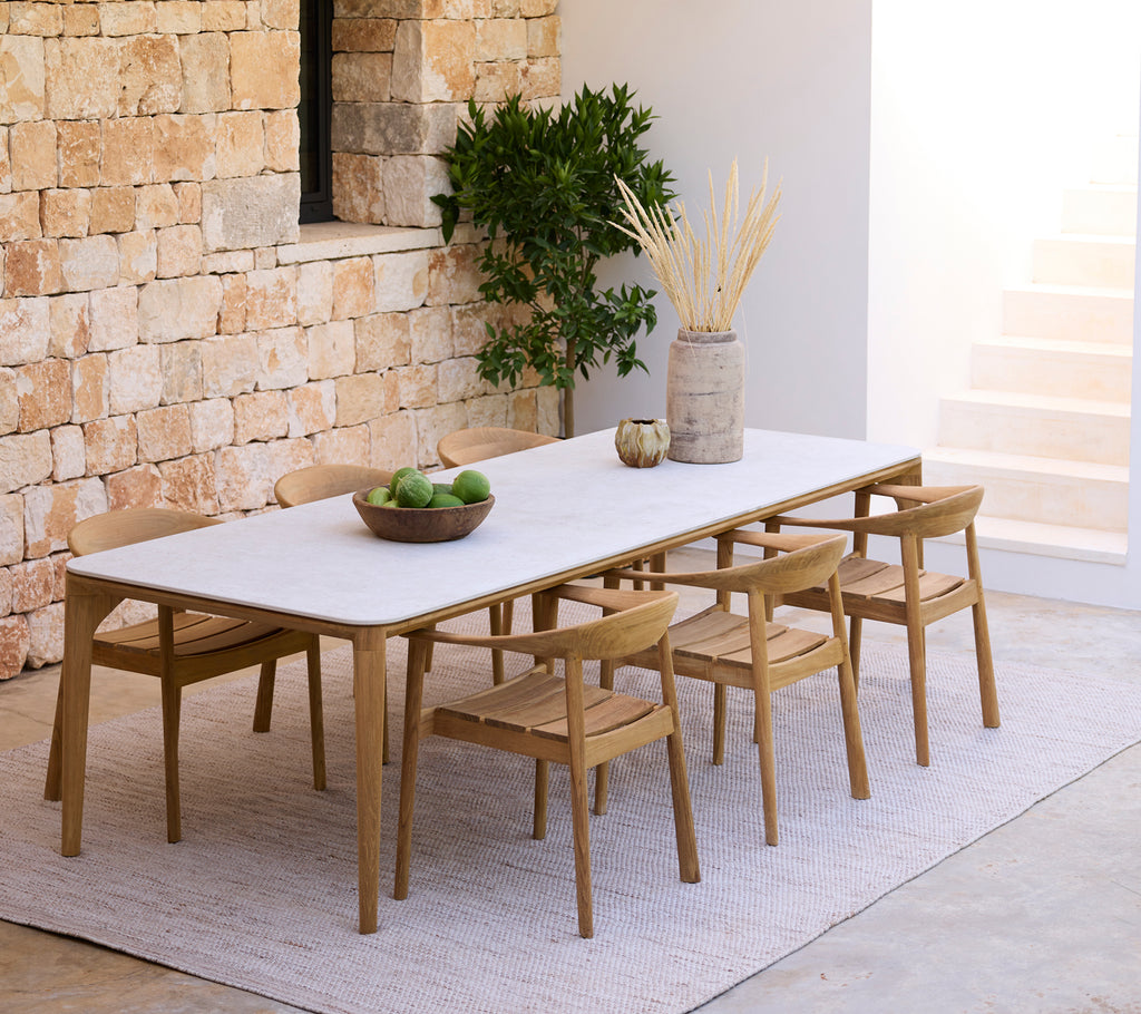 Moderne spisestue med et hvidt bord og træstole mod en stenvæg.