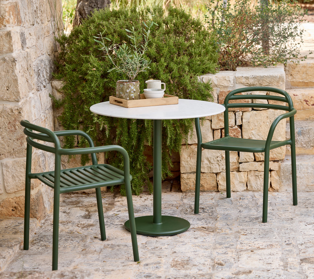 Moderne udendørs indretning med grønne stole og et hvidt bord.