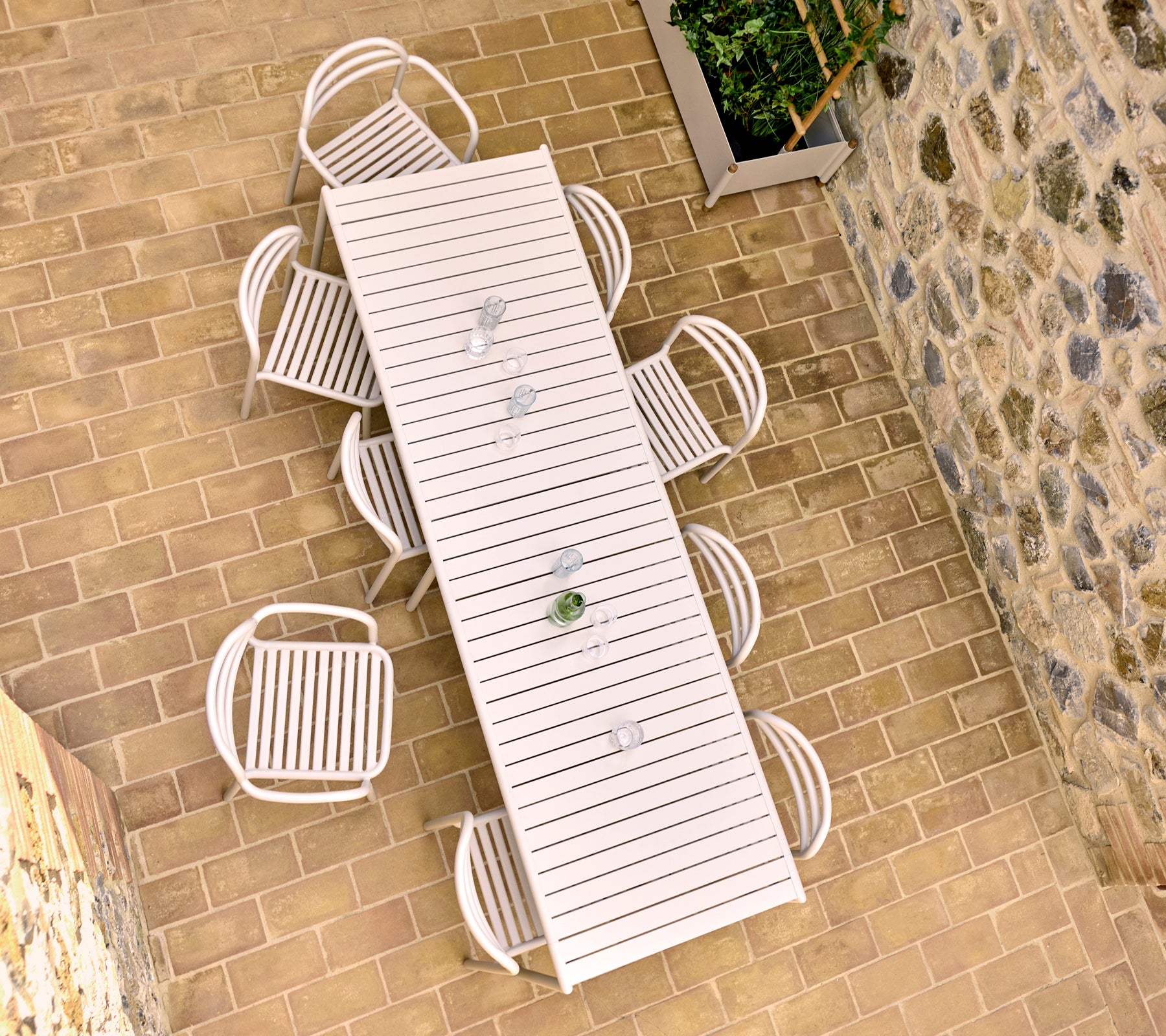 Fugleperspektiv af et sandfarvet udendørs spisebord med otte Bliss stole, placeret på en stenbelagt patio.