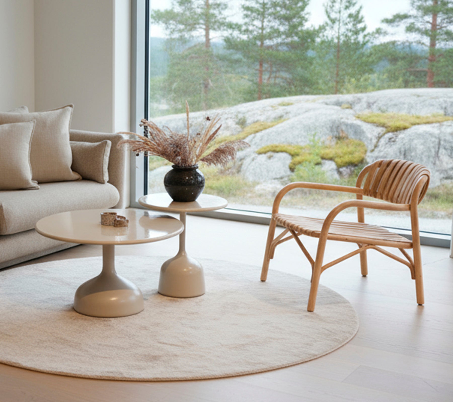 Moderne stue med en sofa, rundt bord, sort vase og rattan stol nær et stort vindue.