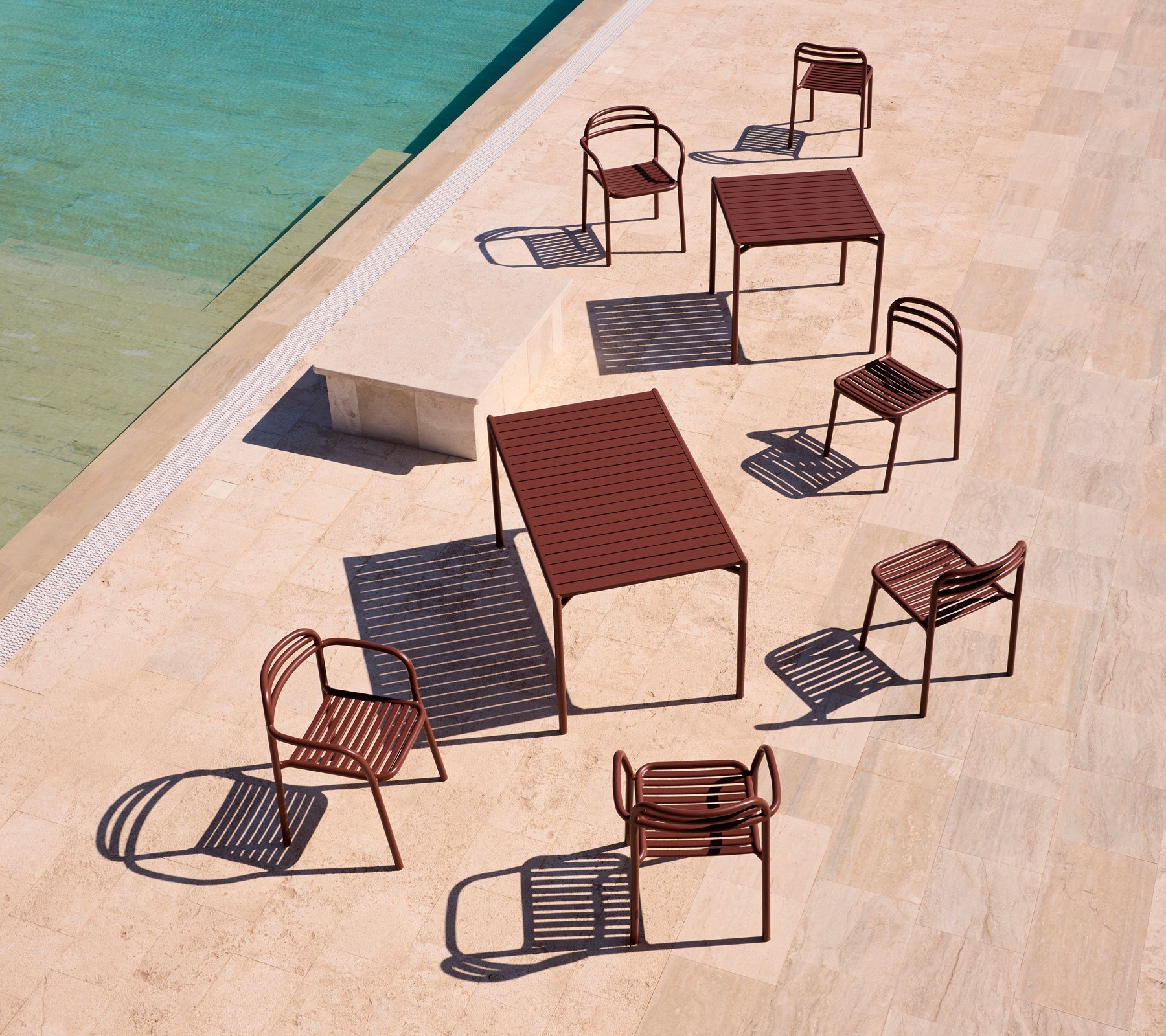 Bliss serien udendørs møbler i ørkenrød, arrangeret omkring en pool på en solbeskinnet terrasse, som kaster legesyge skygger.