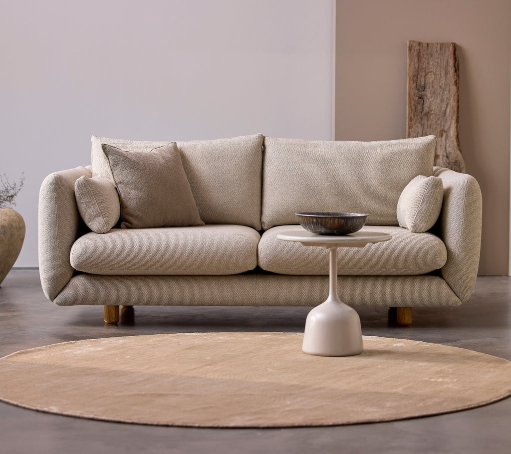 Bloom 2-personers sofa i ørken sand med afdæmpede puder og ben i teak, parret med et minimalistisk sidebord på et rundt tæppe.