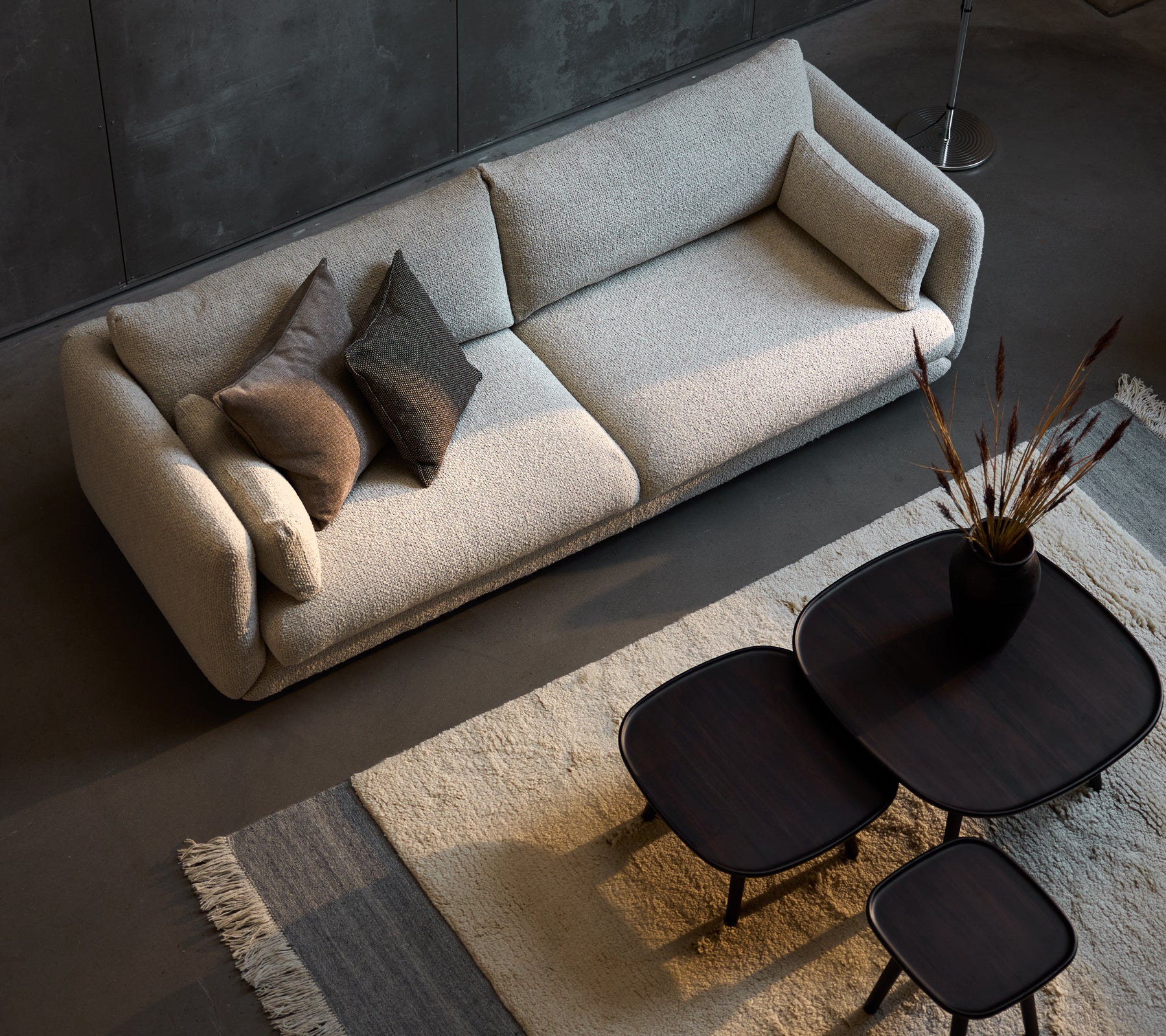 Stilfuld tre-personers sofa i sandfarve, suppleret af tre størrelser af slanke sorte sofaborde og dekorative puder.