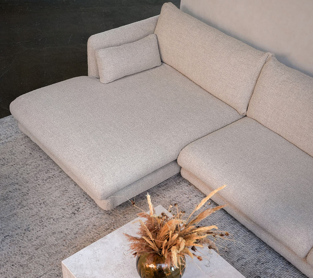 Moderne beige sofa med et hvidt bord og en dekorativ vase i en stilfuld loungeindstilling.