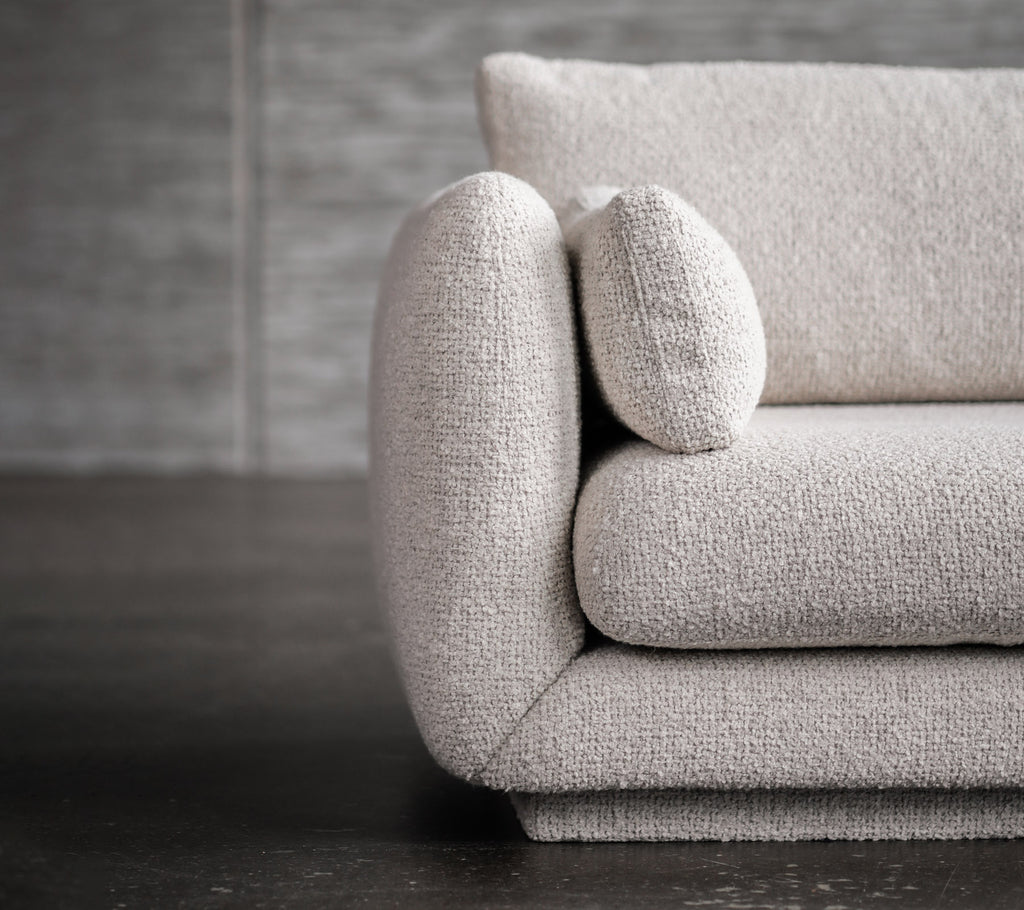 Moderne lysegrå sofa med afrundede armlæn og pude detaljer.