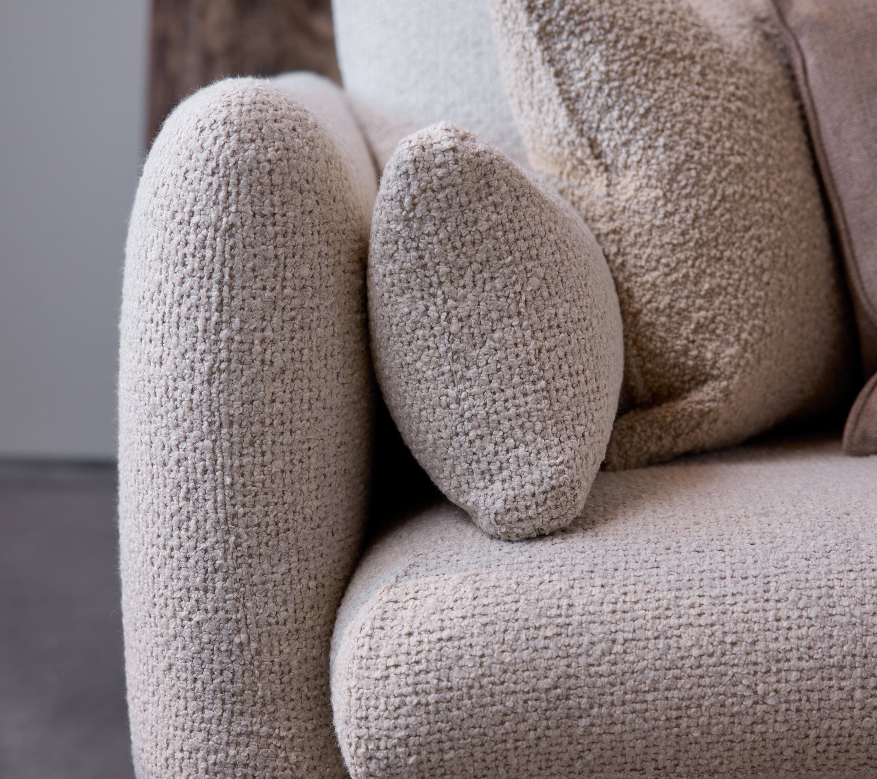 Nærbillede af armlænet på en Bloom-sofa i en sand flair tekstur, der fremhæver et afrundet design og blødt, hyggeligt stof.