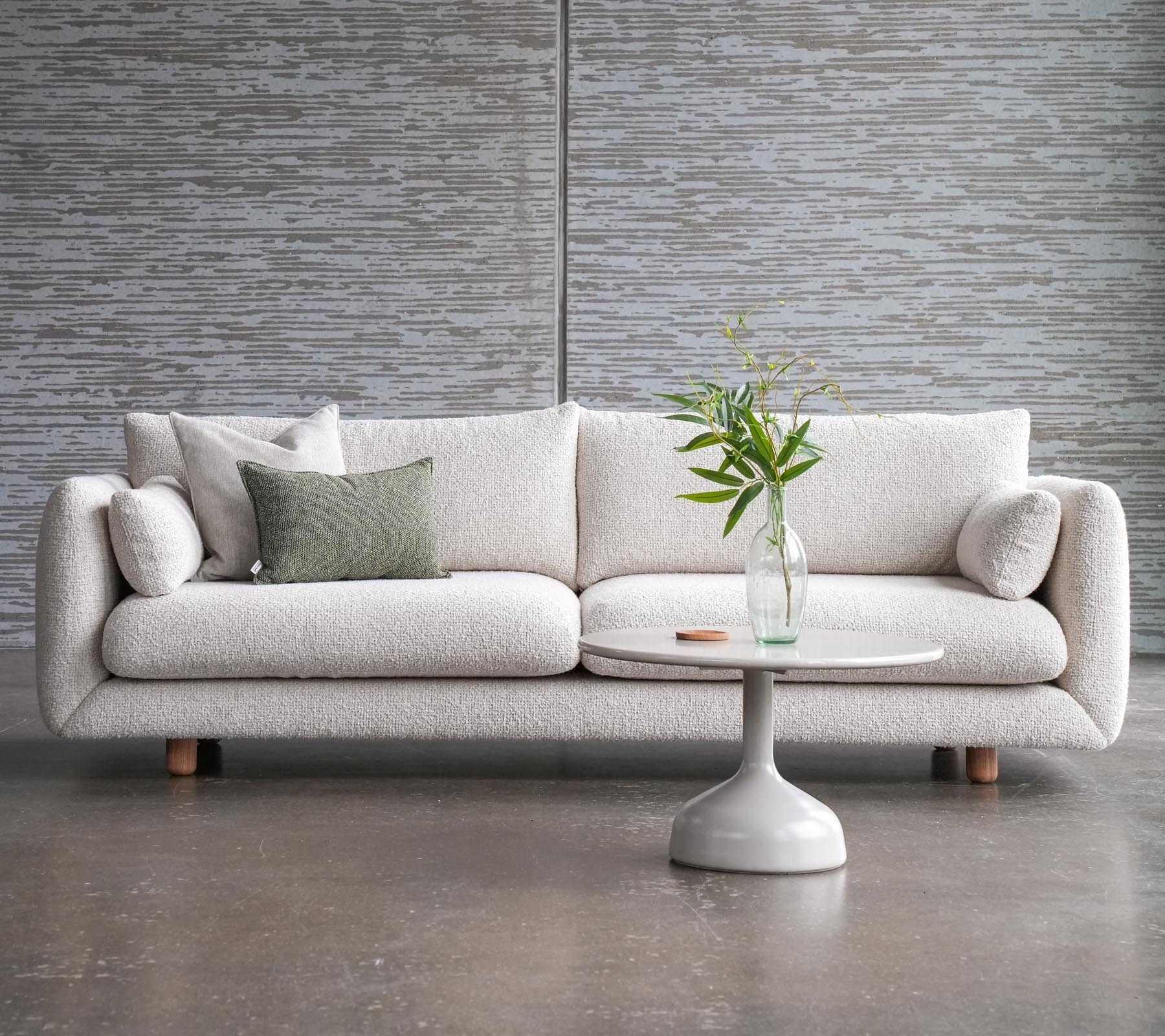 En stilfuld sofa med puder ved siden af et Glaxe kaffebord med en rund top og elegante teakben, prydet med en vase med blomster.