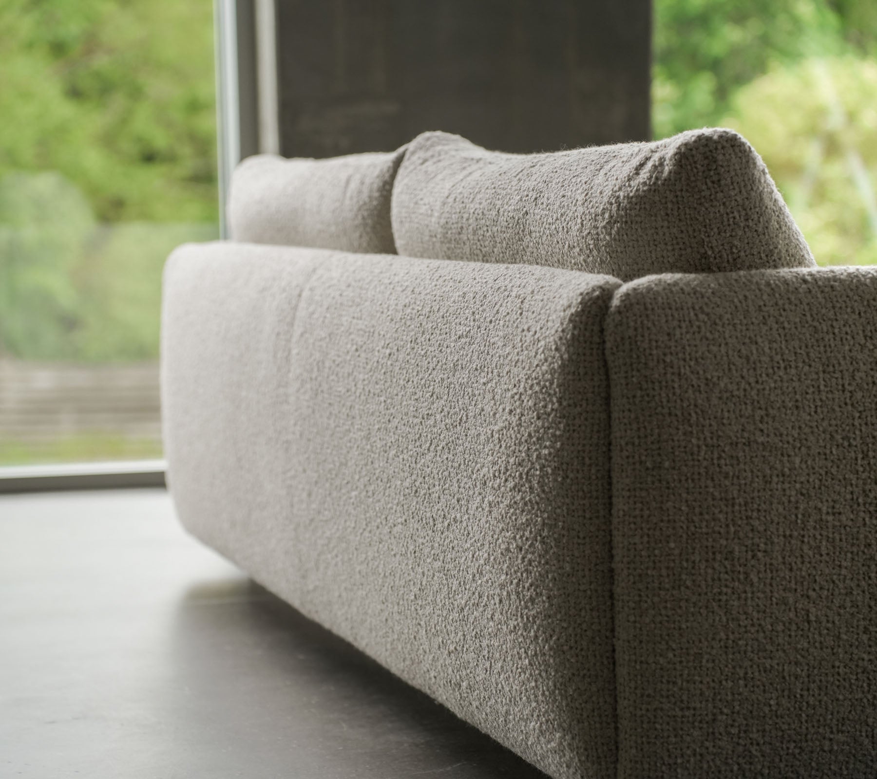 Moderne sofa med en struktureret sandfarvet stof, accentueret af elegante teaktræben, der viser Cane-line flair og bløde puder.