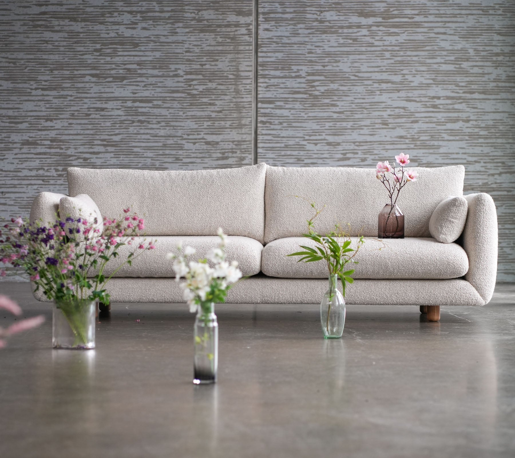 En lysfarvet sofa med teakben, omgivet af vaser med blomster, der viser en blanding af elegance og Cane-line stil.