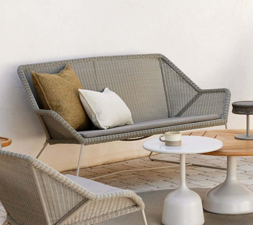 Moderne loungeområde med en grå sofa med puder og runde borde.