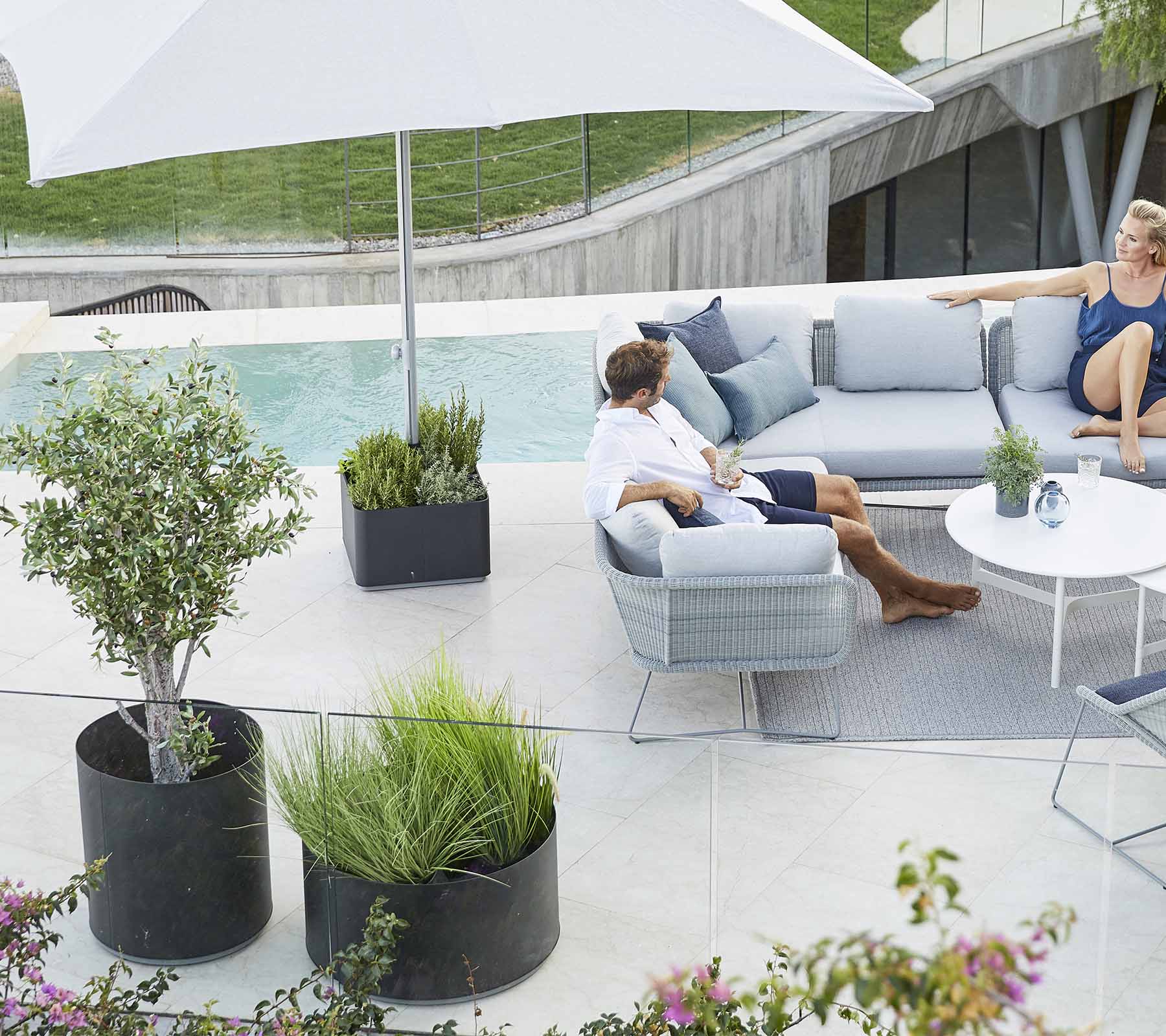 Et stilfuldt udendørs siddeområde med en komfortabel sofa, planter og en stor parasol, perfekt til afslapning.
