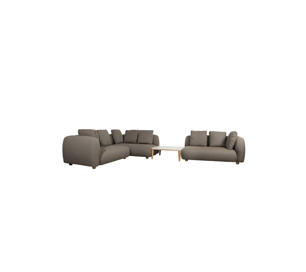 Moderne taupe sofa med puder og et lyst bord i en loungeindstilling.