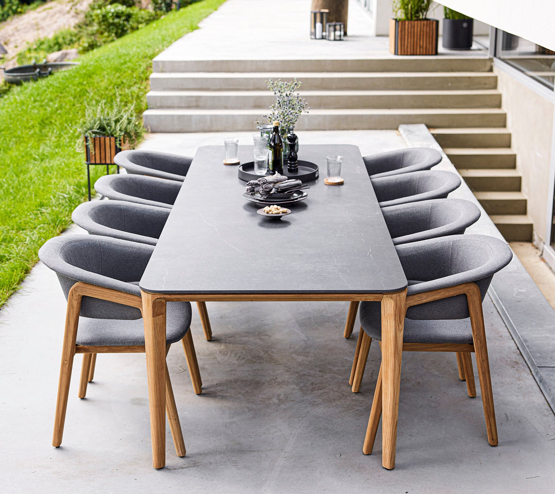 Et moderne spisebord med otte grå stole, der har dekorative genstande og planter på bordet, placeret i et elegant udendørsområde.
