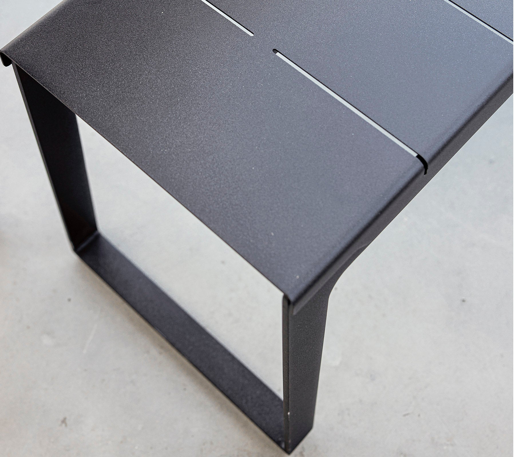 Sort metalbord med et strømlinet design og minimalistisk æstetik, der har en lameloverflade og en robust ramme. Ideel til moderne omgivelser.