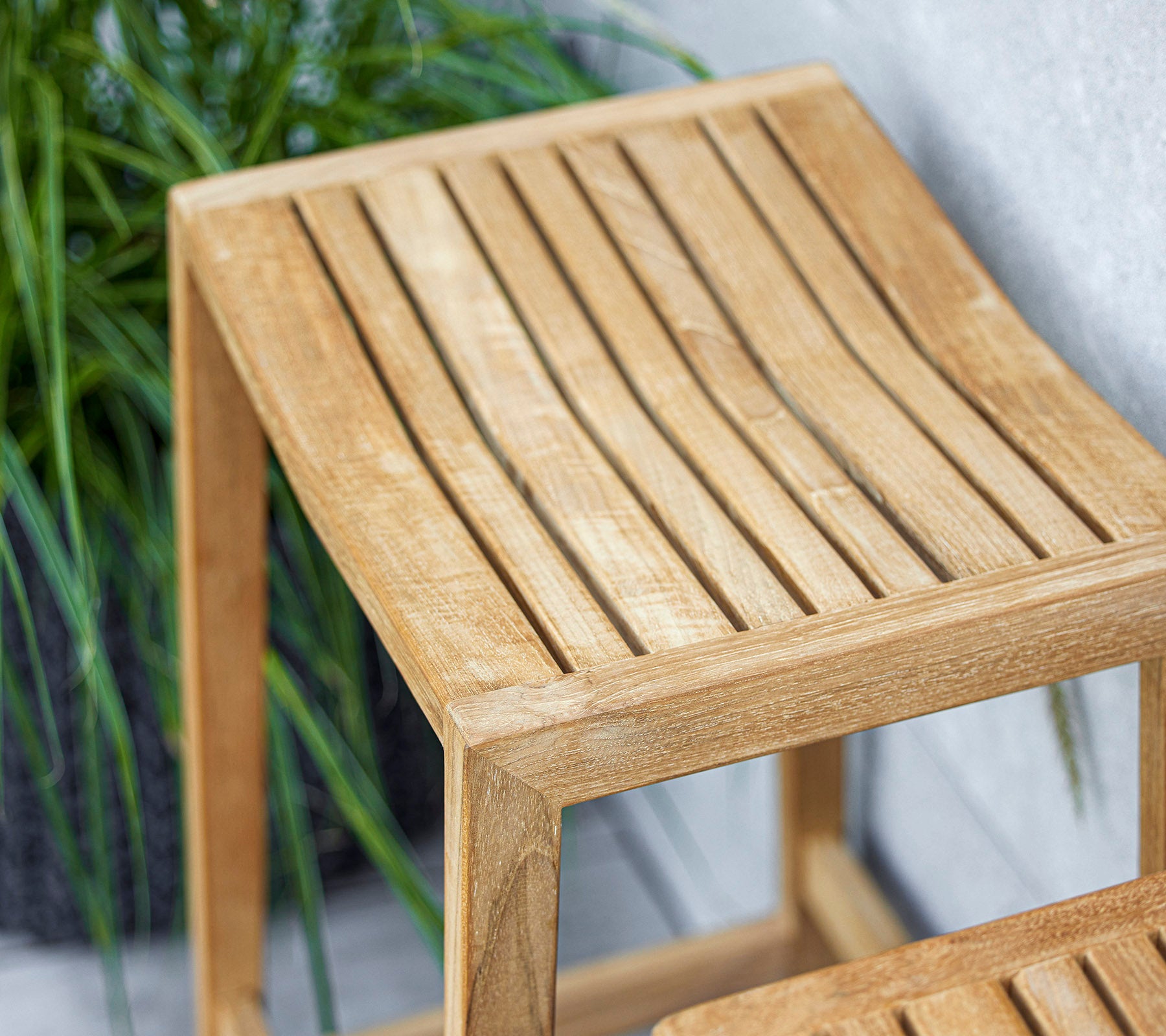 Et elegant træsidebord med et lamel-topdesign, der har en lys finish, der komplementerer den omgivende grønne beplantning.