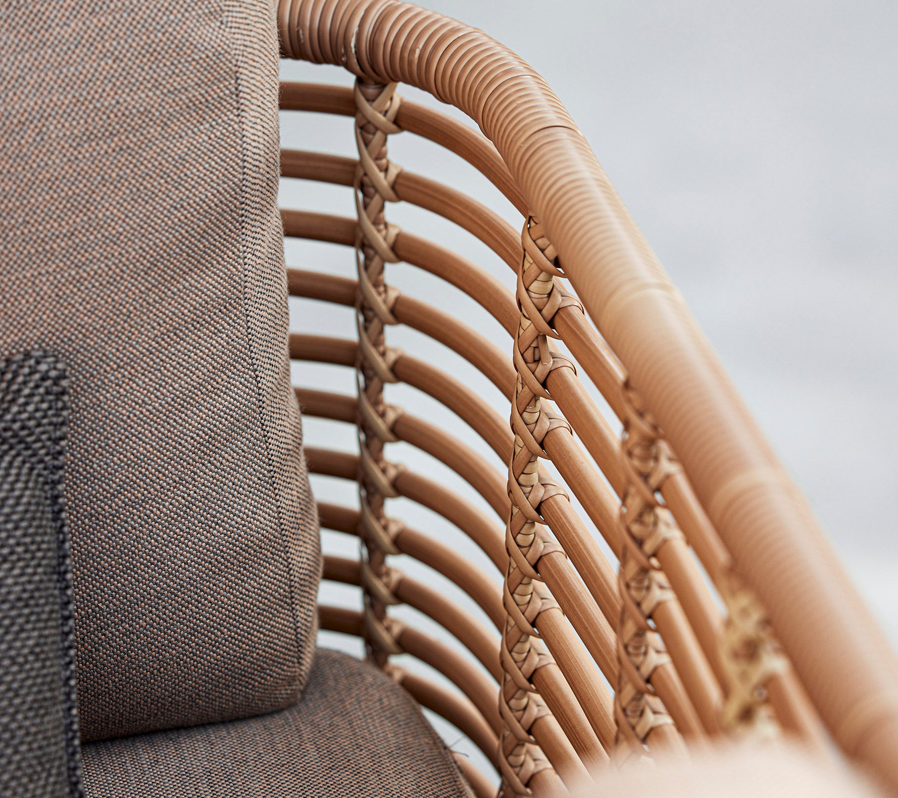 Nærbillede af en stilfuld lænestol med vævede rattan detaljer og bløde puder i neutrale toner, der fremhæver moderne design.