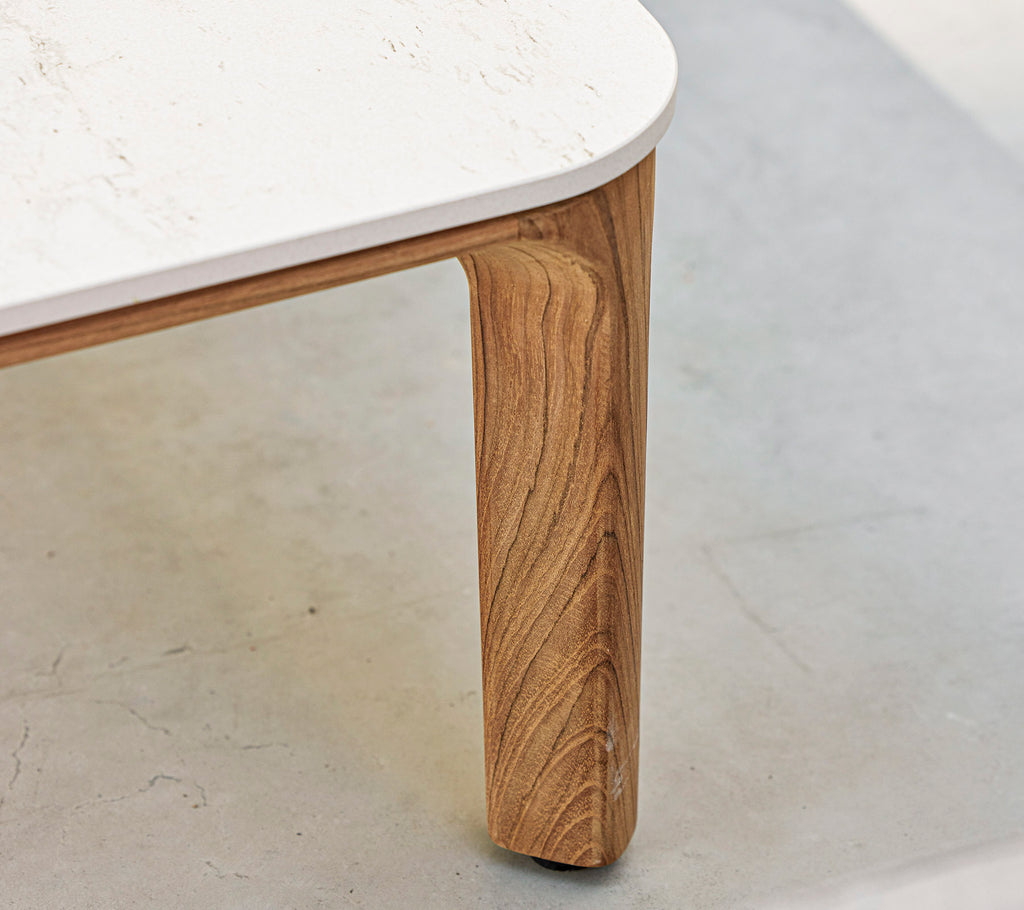 Et nærbillede af et bord med et struktureret træben og en glat, hvid bordplade. Elegante og moderne designelementer fremhæves.