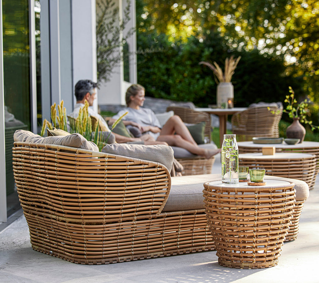 Stilfuldt vævet møbel sæt med et hyggeligt siddeområde og borde, komplementeret af dekorative planter og en afslappet atmosfære.
