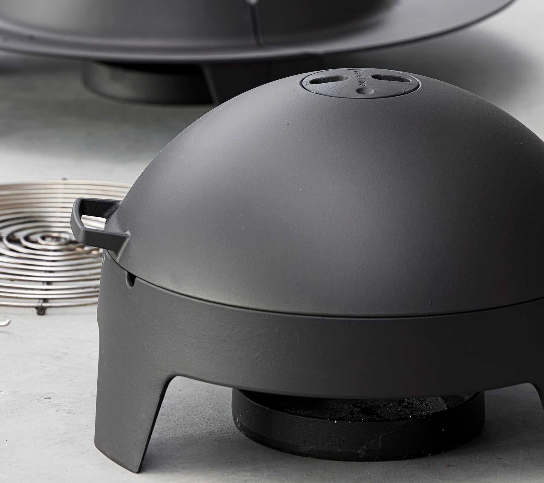 Matte sort madlavningsapparat med en kuppelformet låg og en aftagelig varmekilde, designet til udendørs grillning og barbecue.