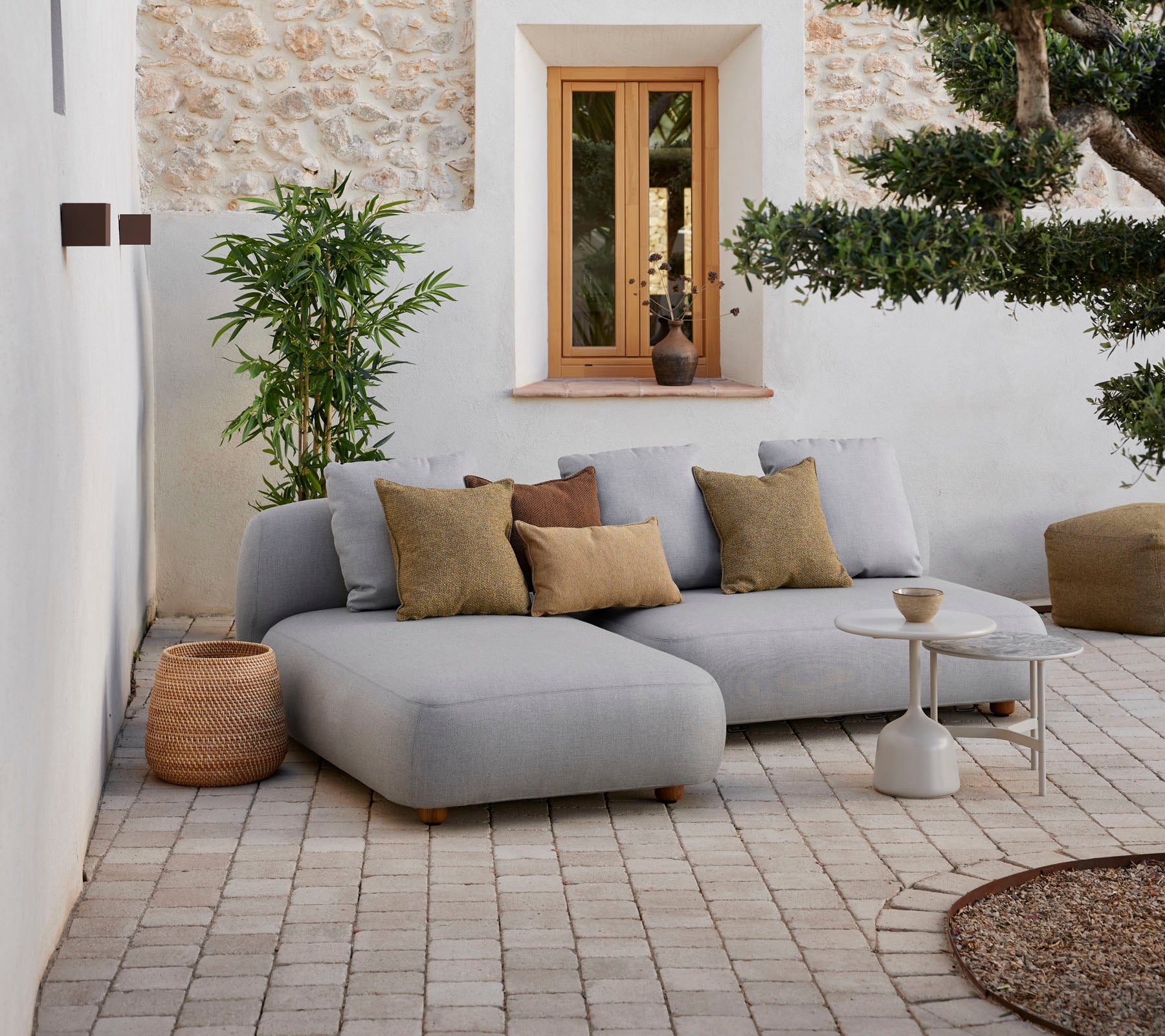 Moderne grå sektionel sofa med dekorative puder, lille sidebord og naturlige elementer i en hyggelig indstilling.