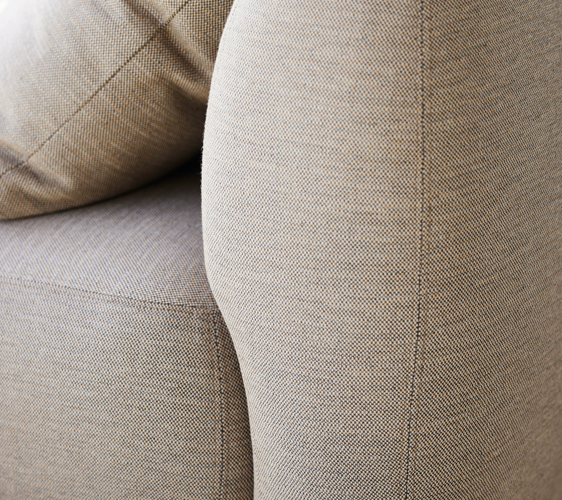 Nærbillede af en tekstureret beige polstring, der fremhæver den buede armlæn og bløde puder på et møbel.