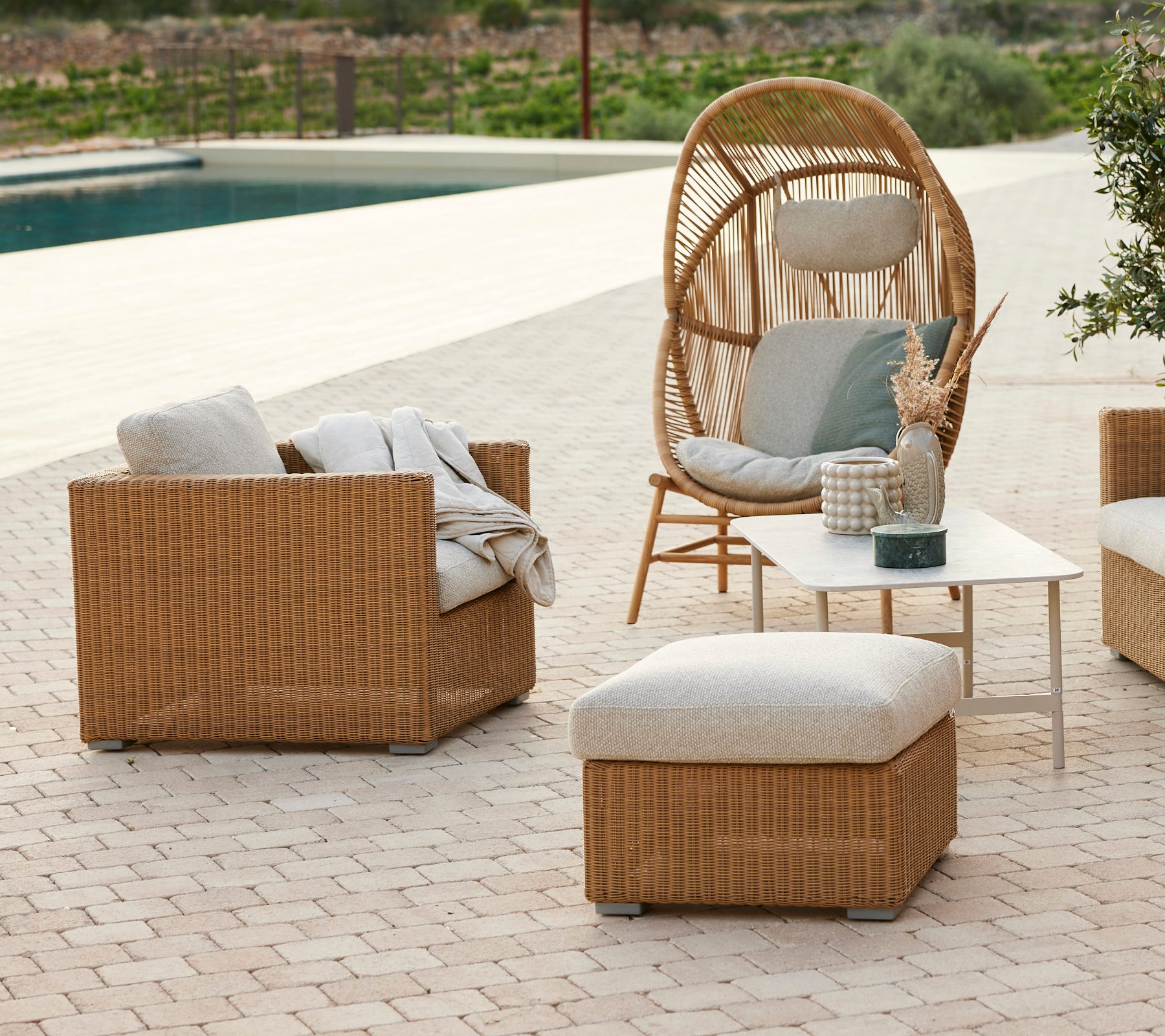Moderne loungeområde med en rattan stol, grå puder, rattan sofa og et kaffebord.