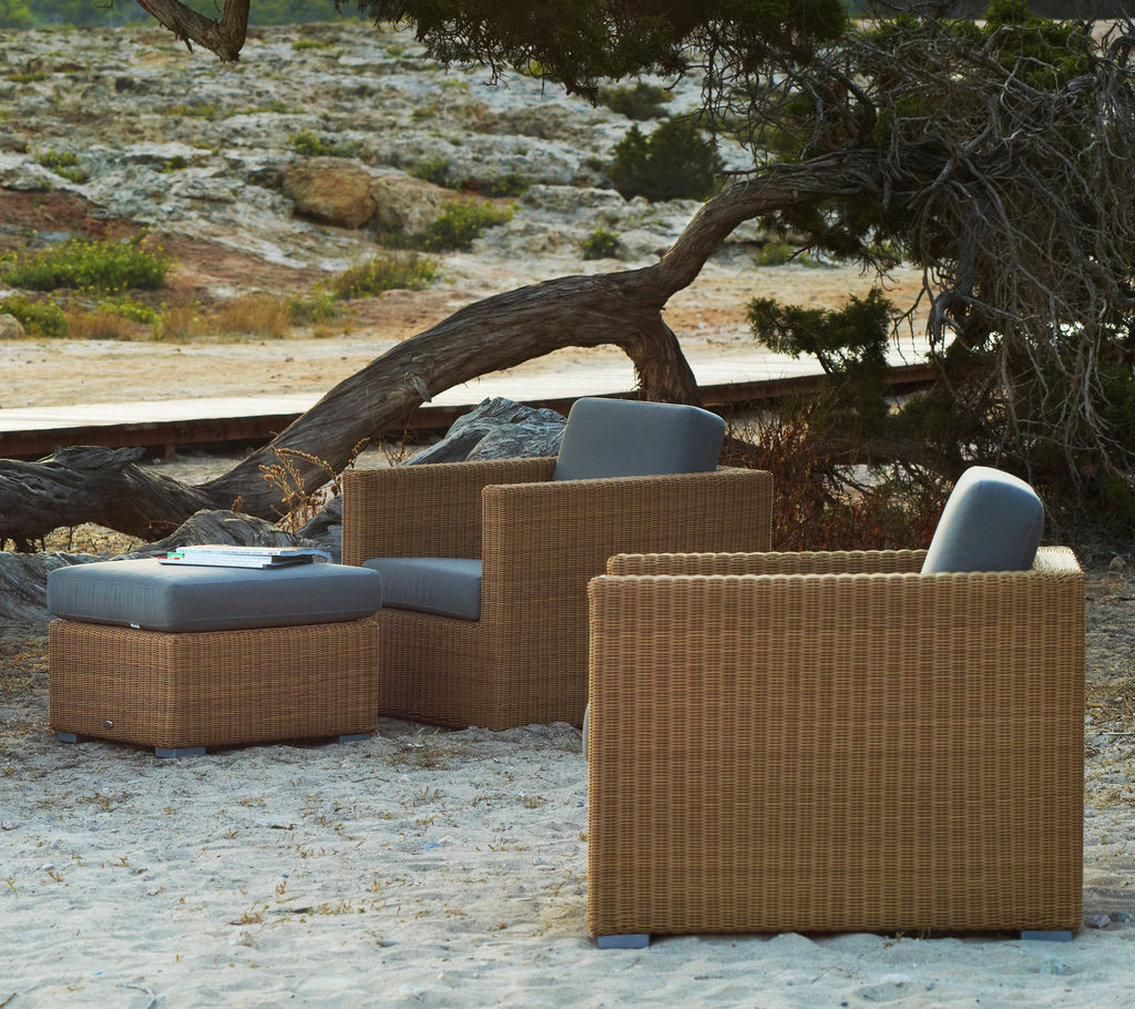 Rattan loungestole med grå puder i en naturlig udendørs indstilling.