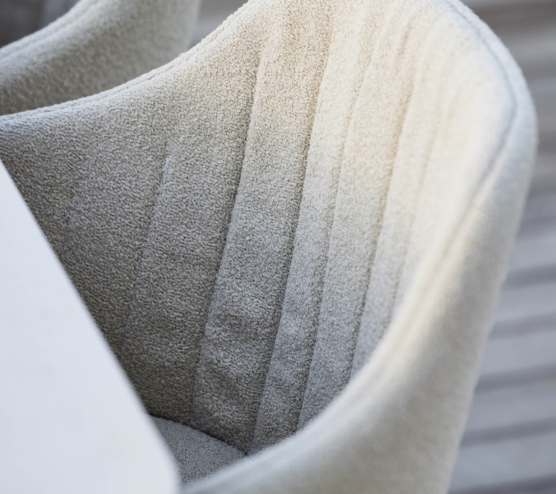 Tekstilbetrukket, fuldpolstret stol med diskret lodret syning, der viser en blød, neutral farve og et moderne designæstetik.