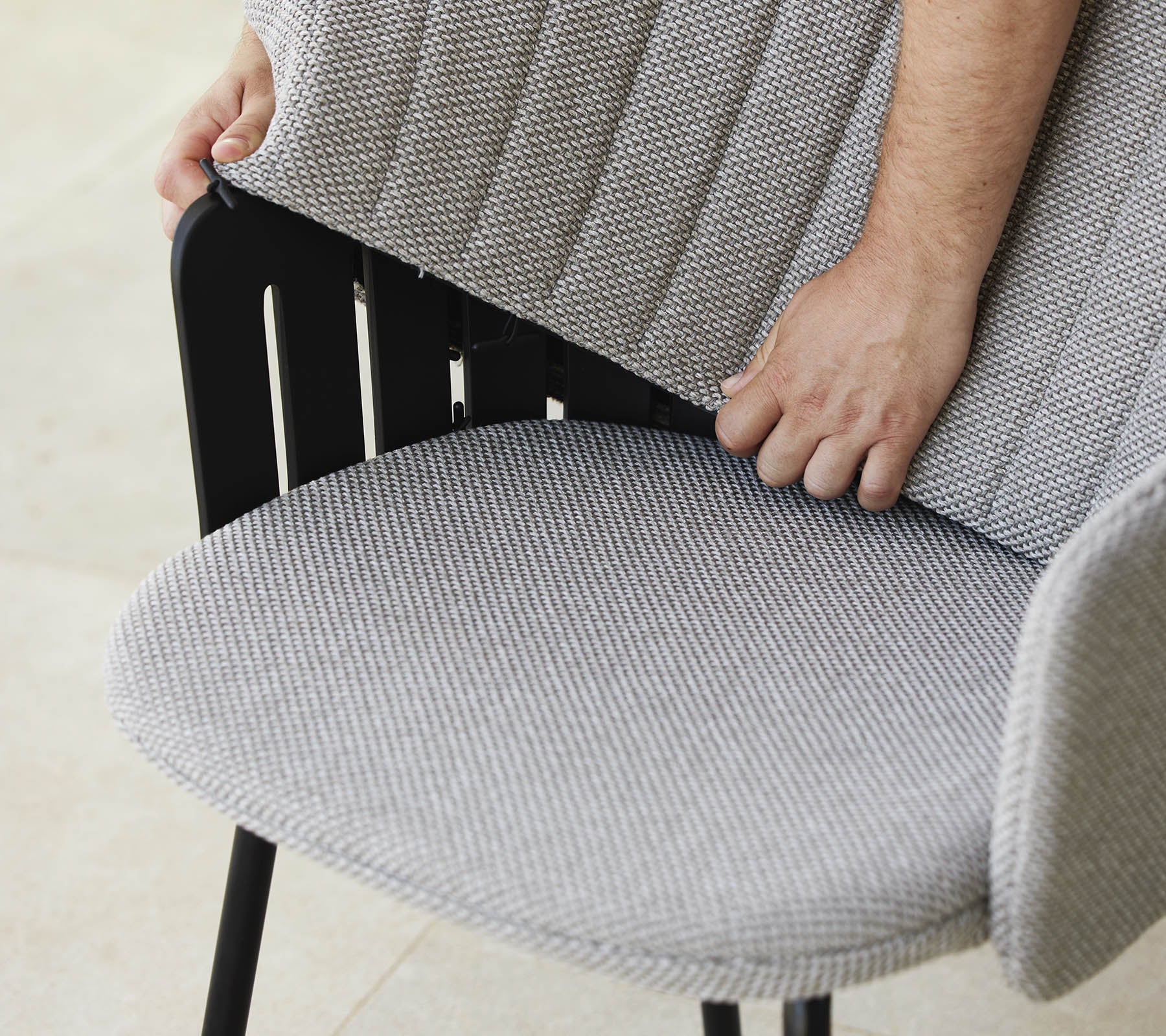 Person justerer ryggen på en moderne stol med et tekstureret stofsæde, som viser et stilfuldt design og ergonomisk støtte.