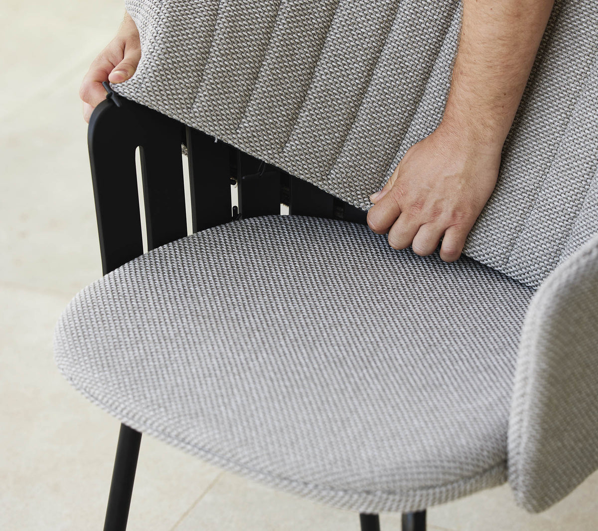 Person justerer ryggen på en moderne stol med et tekstureret stofsæde, som viser et stilfuldt design og ergonomisk støtte.