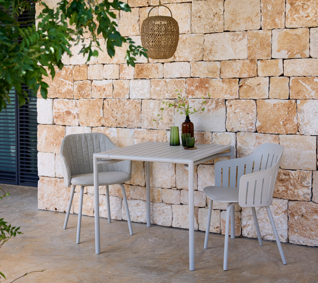 Moderne grå bord og stole med grønne og brune flasker i en udendørs omgivelser.