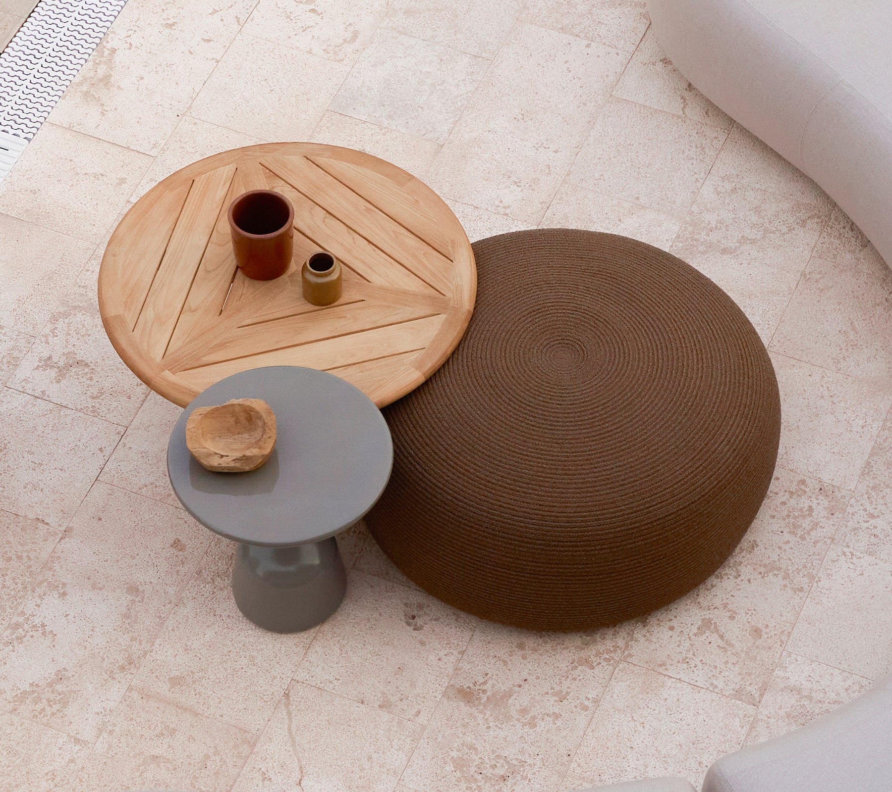 Et stort, rundt fodskammel i brun ved siden af et trækaffe bord med et geometrisk design, der har små dekorative genstande ovenpå.
