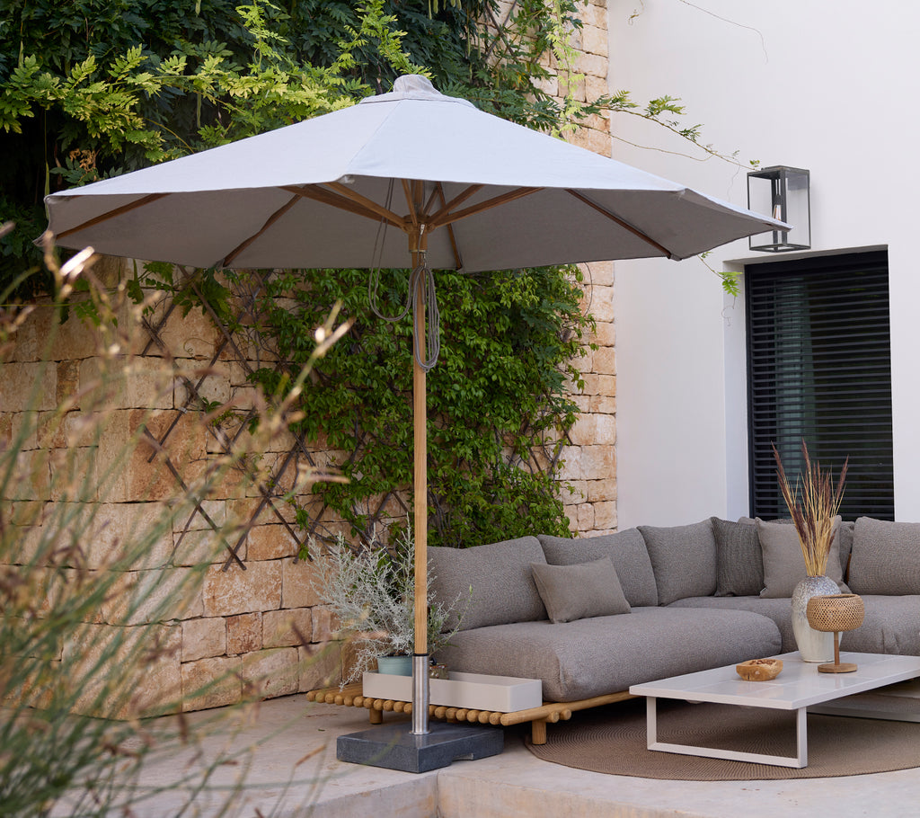 Moderne loungeområde med en grå sofa, hvidt bord og grå parasol.