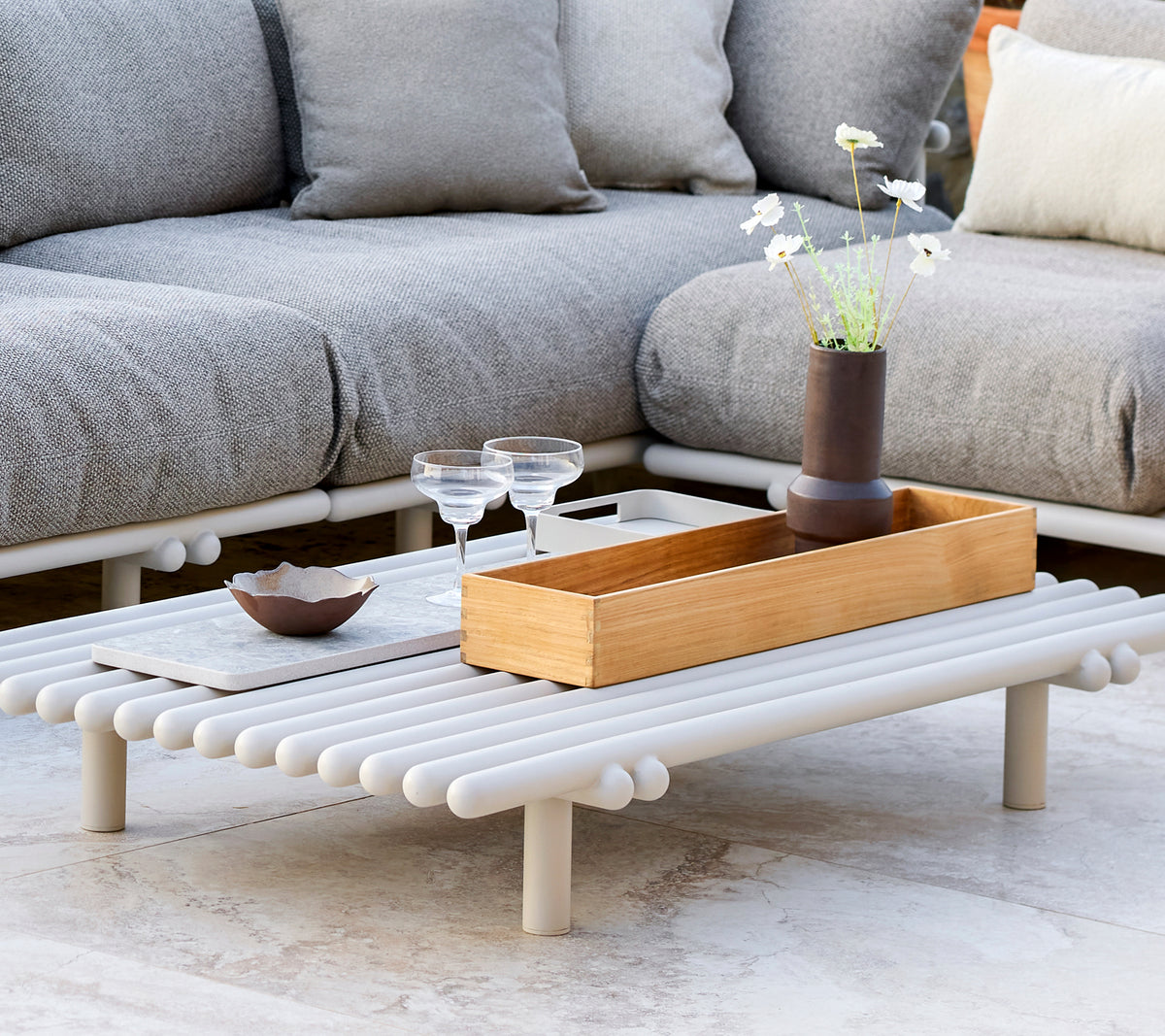 Et stilfuldt kaffebord med en teak opbevaringsboks, der har et minimalistisk design og dekorative elementer som glas og en lille vase.