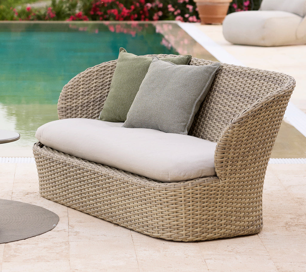 Kyst lounge sofa med bløde puder, med et vævet design i en sandfarve, perfekt til afslapning ved poolen.