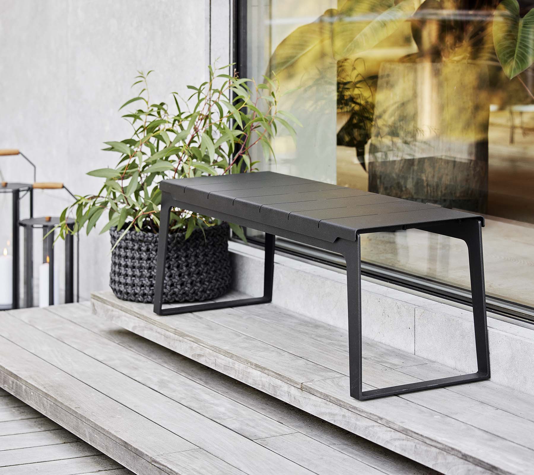 En slank sort bænk placeret ved siden af en plantekasse med grønne planter, der viser moderne designelementer og minimalistisk æstetik.